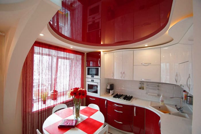Красно-белый интерьер кухни смотрится интересно за счёт конструкции самого гарнитура и повторения его геометрической формы на потолке