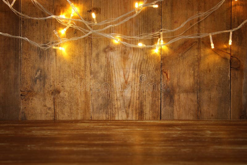 Wood board table in front of Christmas warm gold garland lights on wooden rustic background. glitter overlay stock photo